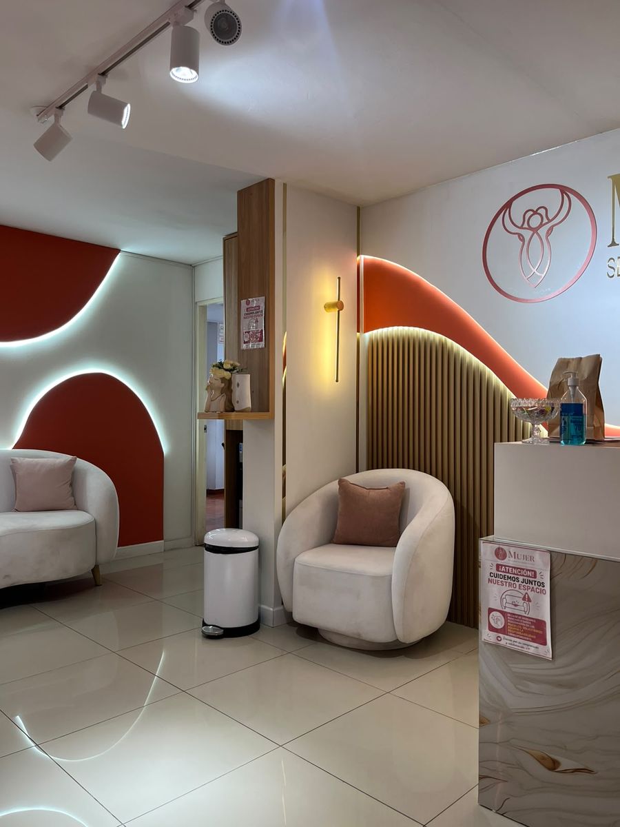 Sala de espera del consultorio, con sillones curvos claros, paredes en terracota y paneles de madera