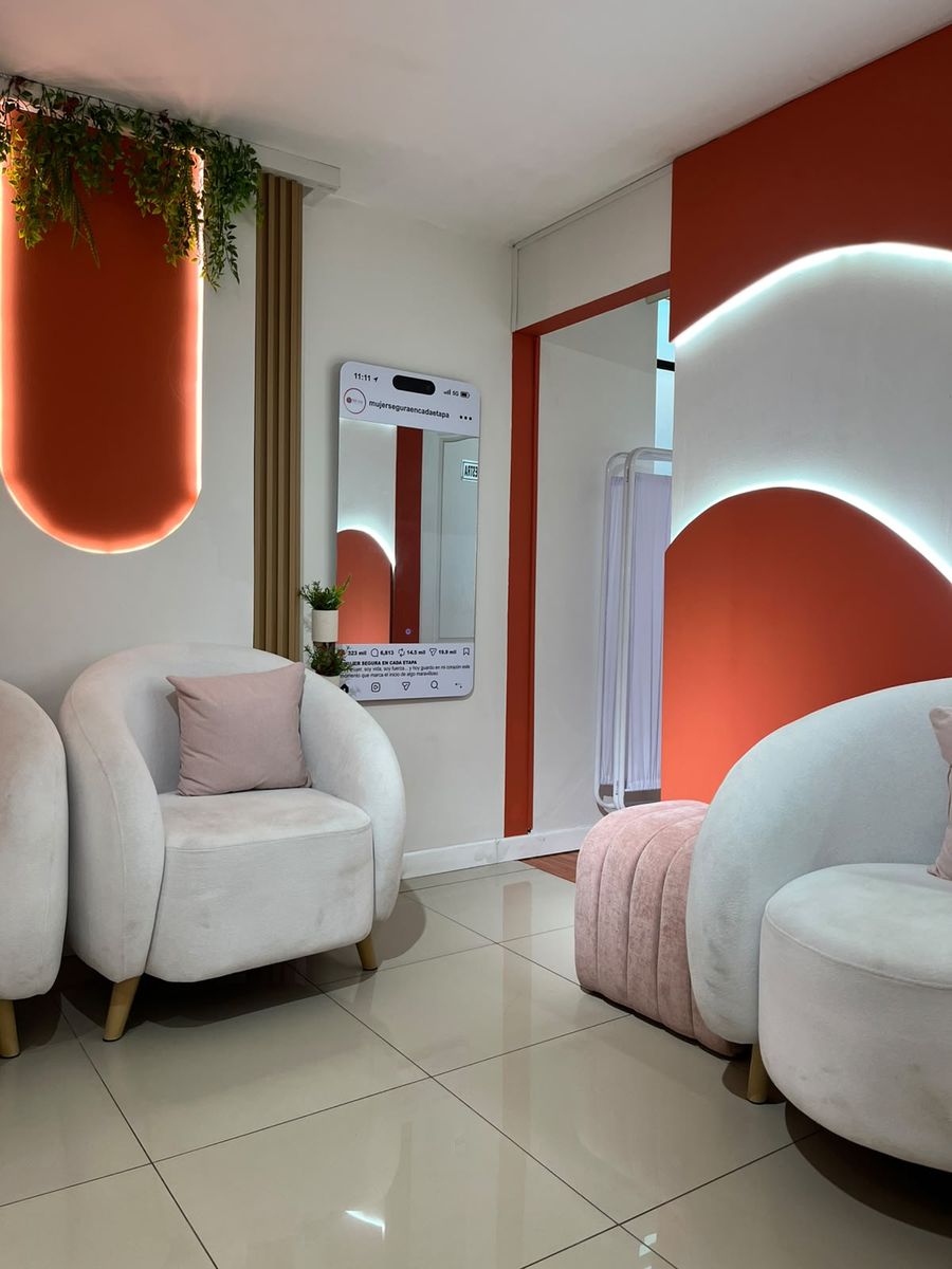 Sala de espera con sillones redondeados, arcos iluminados en terracota y plantas colgantes
